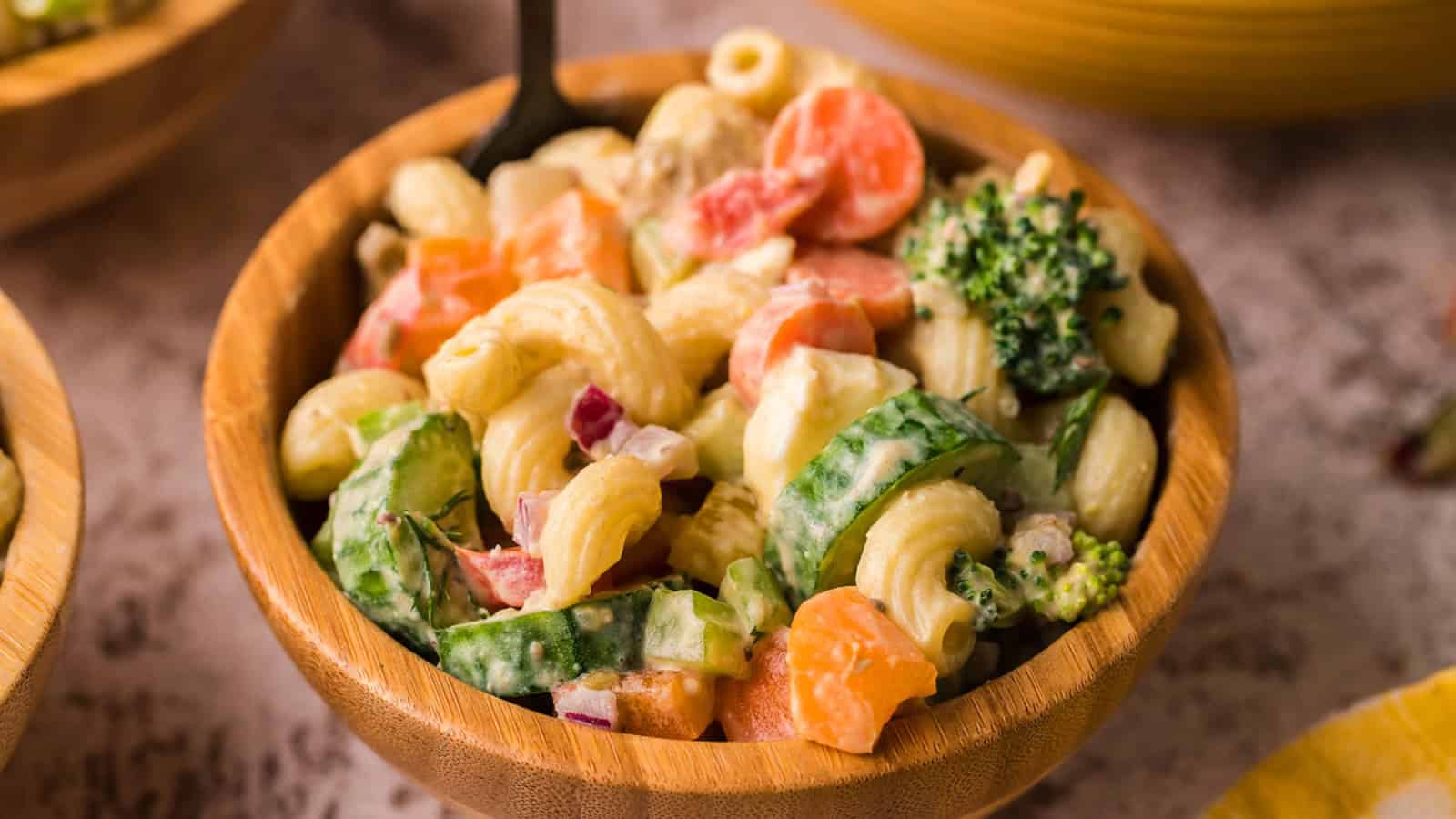Pasta salad with cucumbers, broccoli, carrots, and creamy dressing in a wooden bowl.