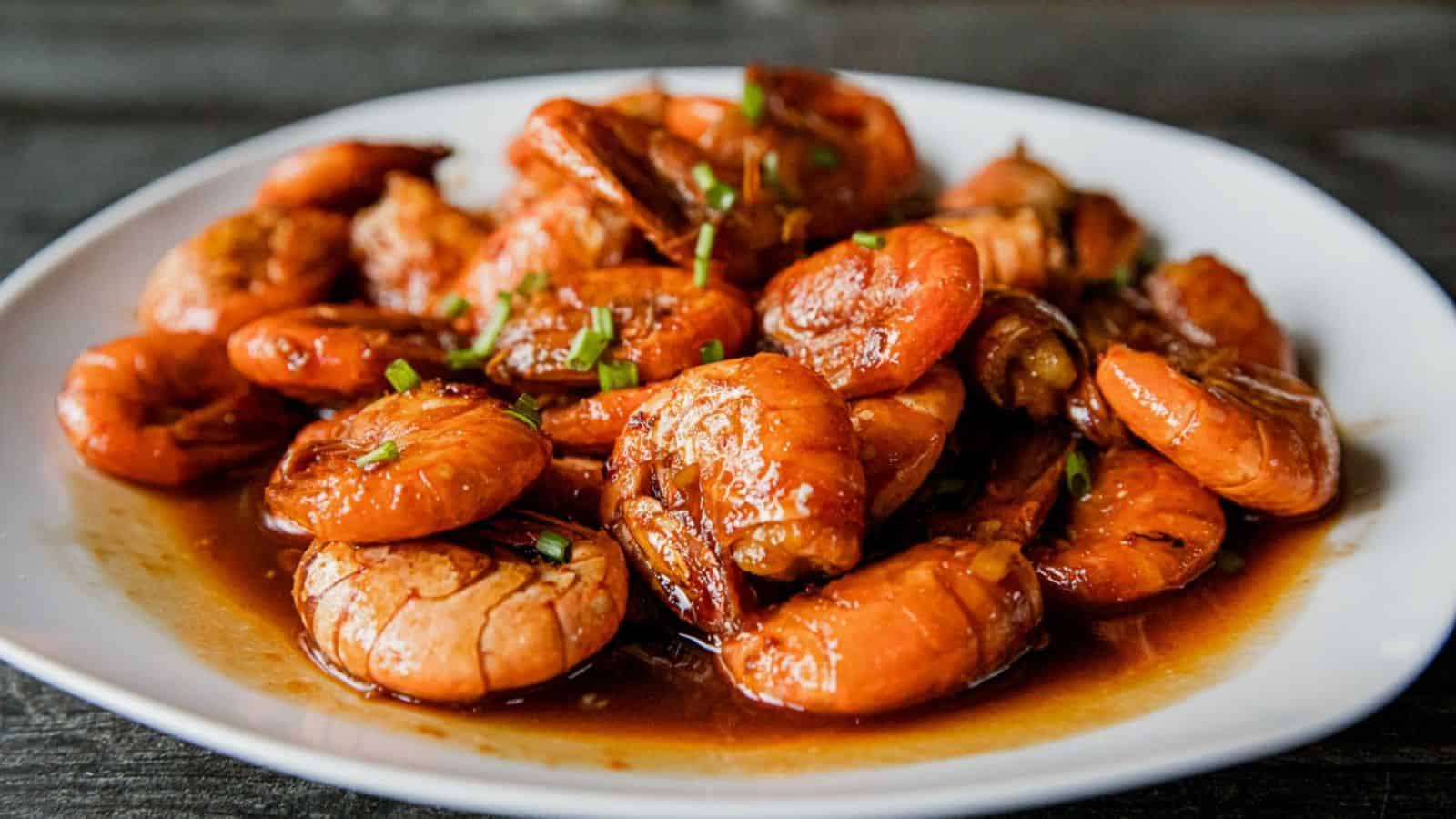 Shrimp cooked in a savory brown sauce, garnished with chopped green onions, served on a white plate.