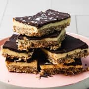 Stack of chocolate, coconut, and cream layered dessert bars on a pink plate.