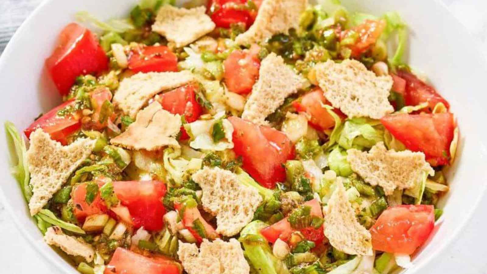 A bowl of salad with chopped tomatoes, lettuce, pita chips, and green herb dressing.