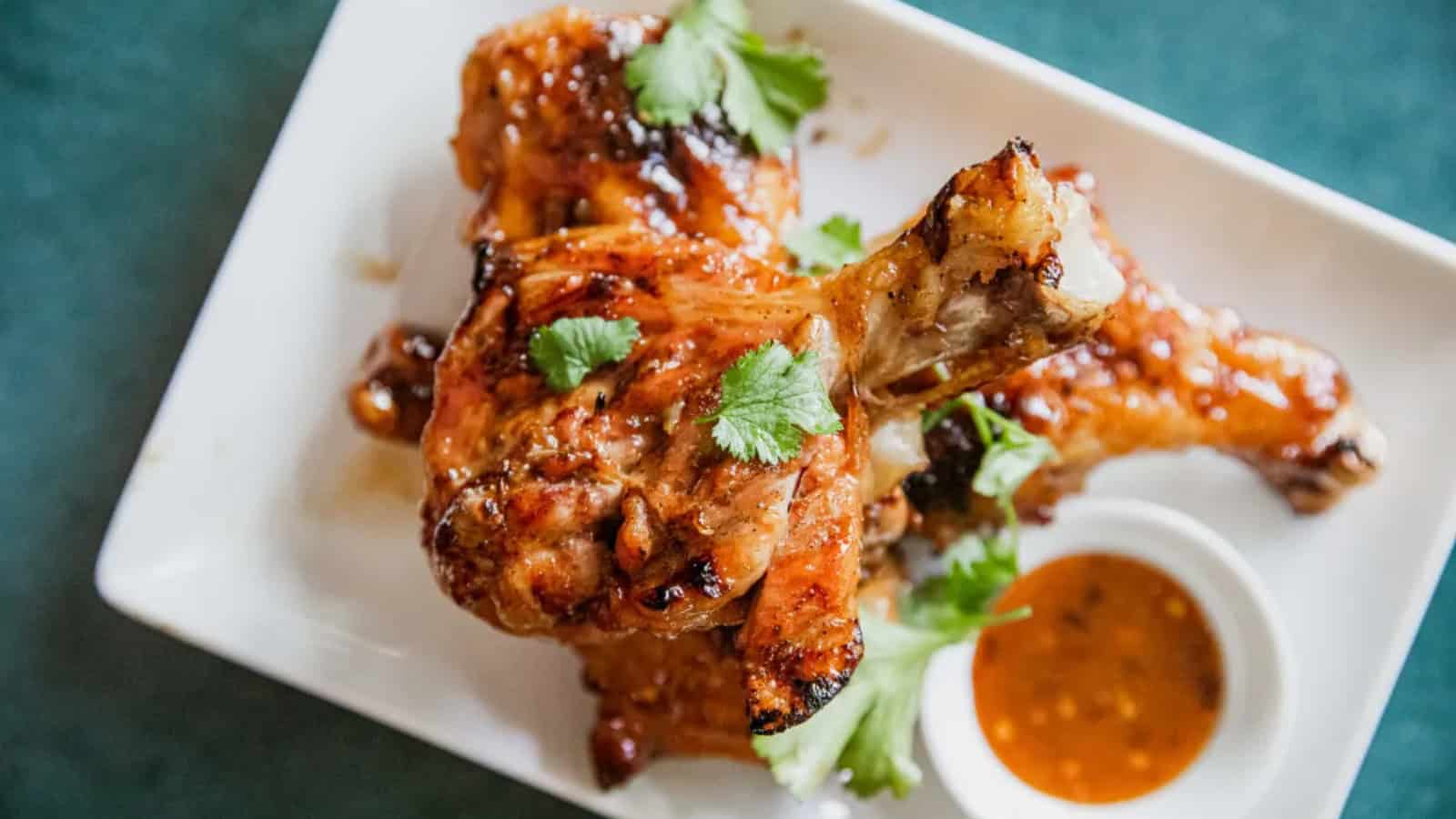 Grilled chicken drumsticks garnished with cilantro on a white plate, served with a side of dipping sauce.