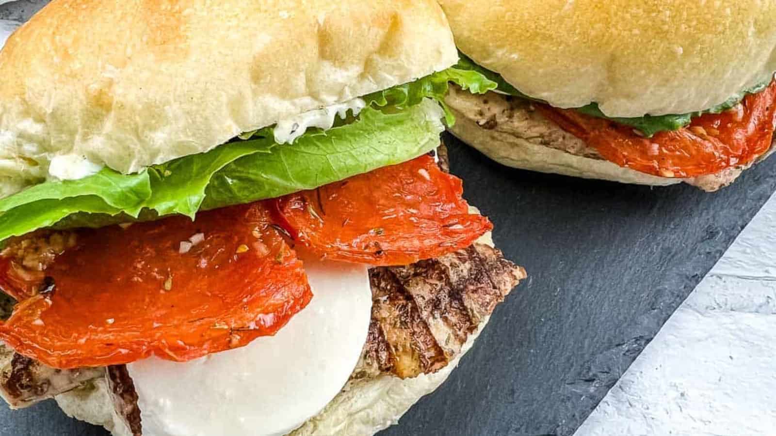 2 Grilled Chicken Caprese Sandwiches on a black plate.