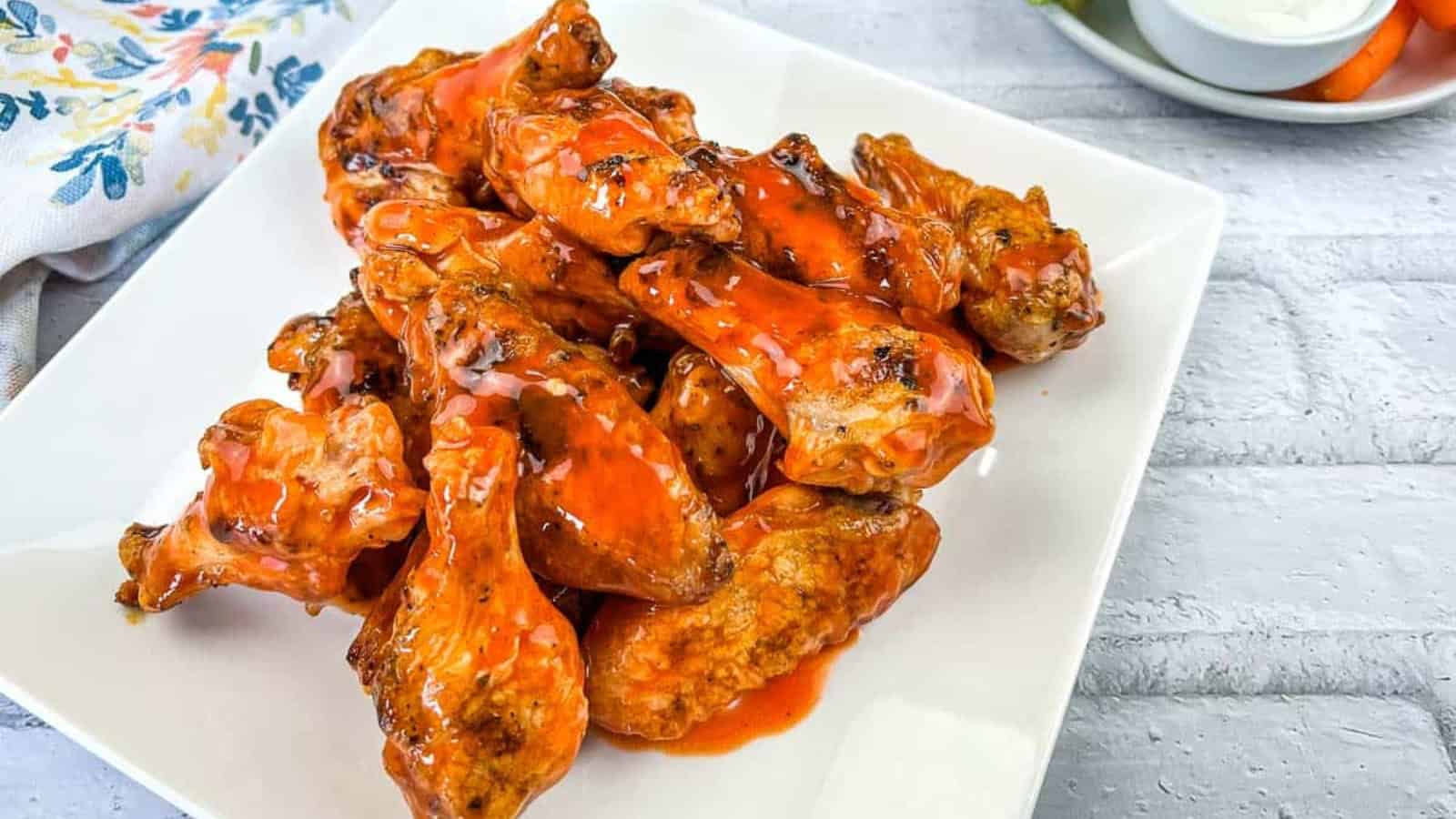 Chicken wings on a white plate with sauce and carrots.