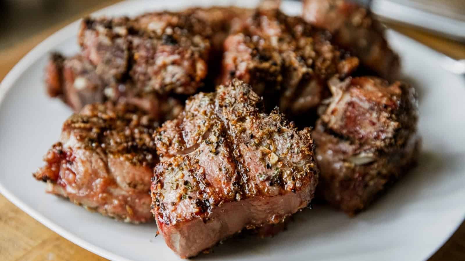 Seasoned and grilled chunks of steak are arranged on a white plate.