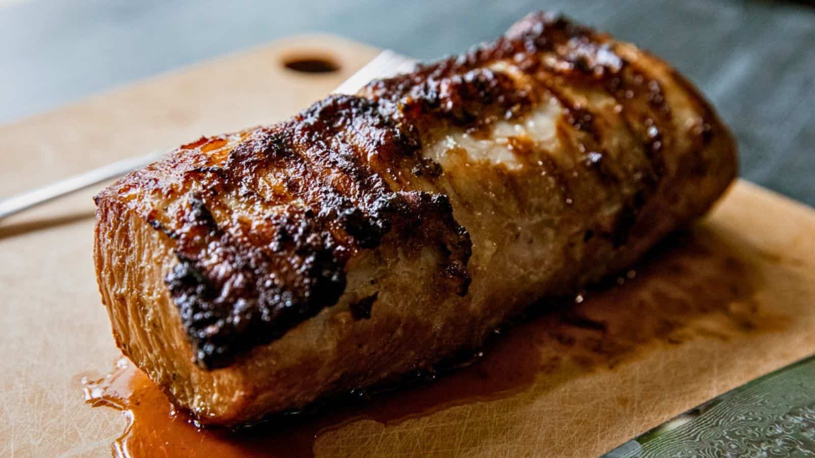 A roasted pork loin with a crispy, golden-brown crust sits on a wooden cutting board.