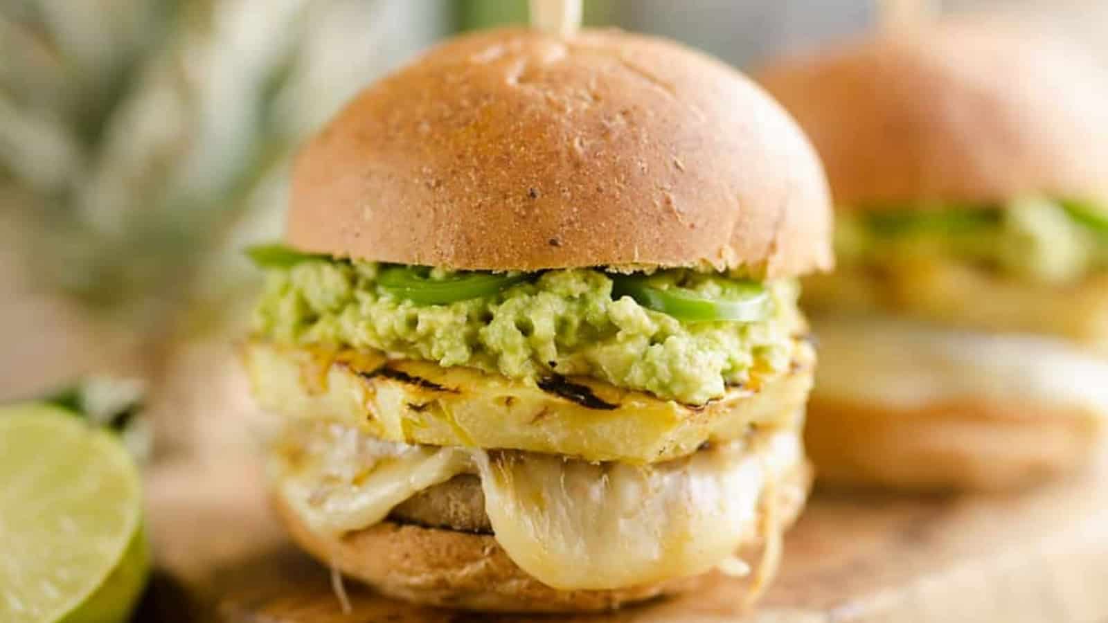 A close-up of a veggie burger with melted cheese, grilled pineapple, guacamole, and jalape&ntilde;o slices.