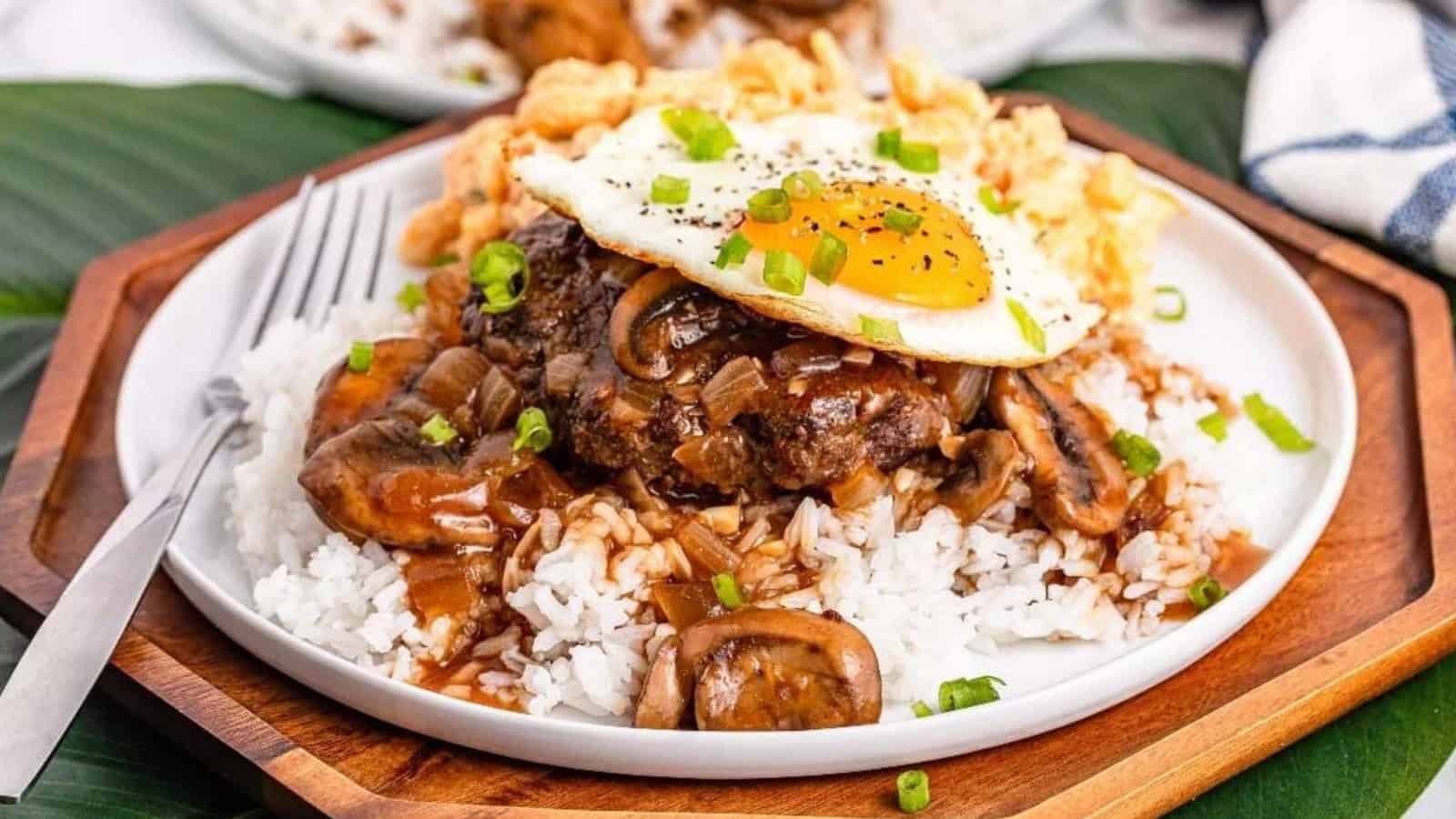 A plate of rice topped with hamburger patty, brown gravy, onions, mushrooms, and a sunny-side-up egg.