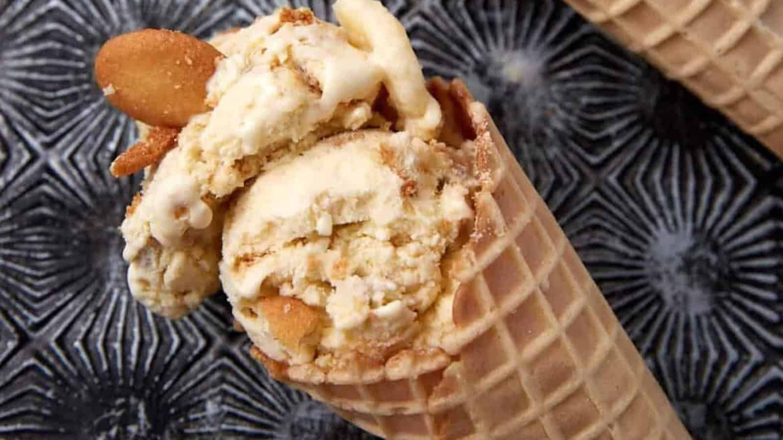 A waffle cone filled with vanilla ice cream and cookie pieces on a patterned black surface.
