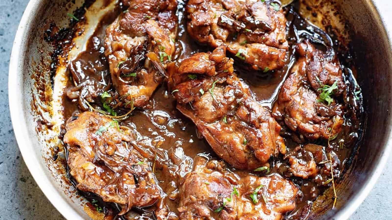Chicken thighs in a skillet with rich brown sauce and herbs, cooked to a golden-brown finish.