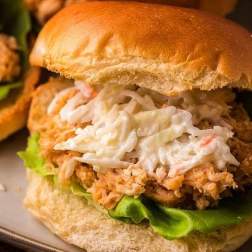 Pulled chicken sandwich with lettuce and creamy coleslaw on a bun, served on a plate.