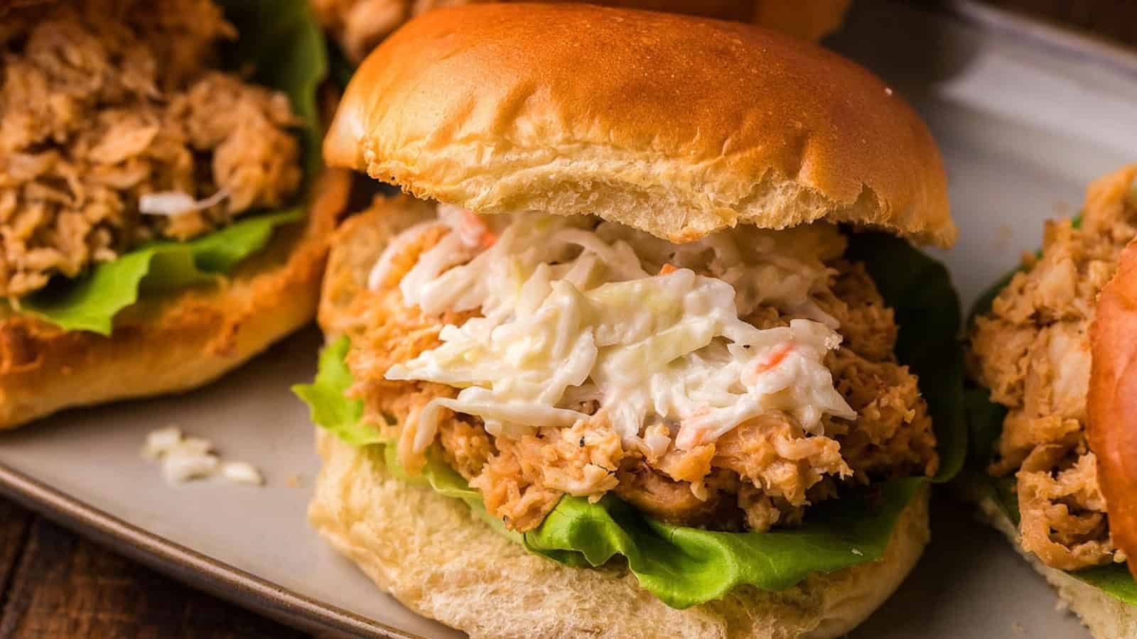 Pulled chicken sandwich with lettuce and creamy coleslaw on a bun, served on a plate.