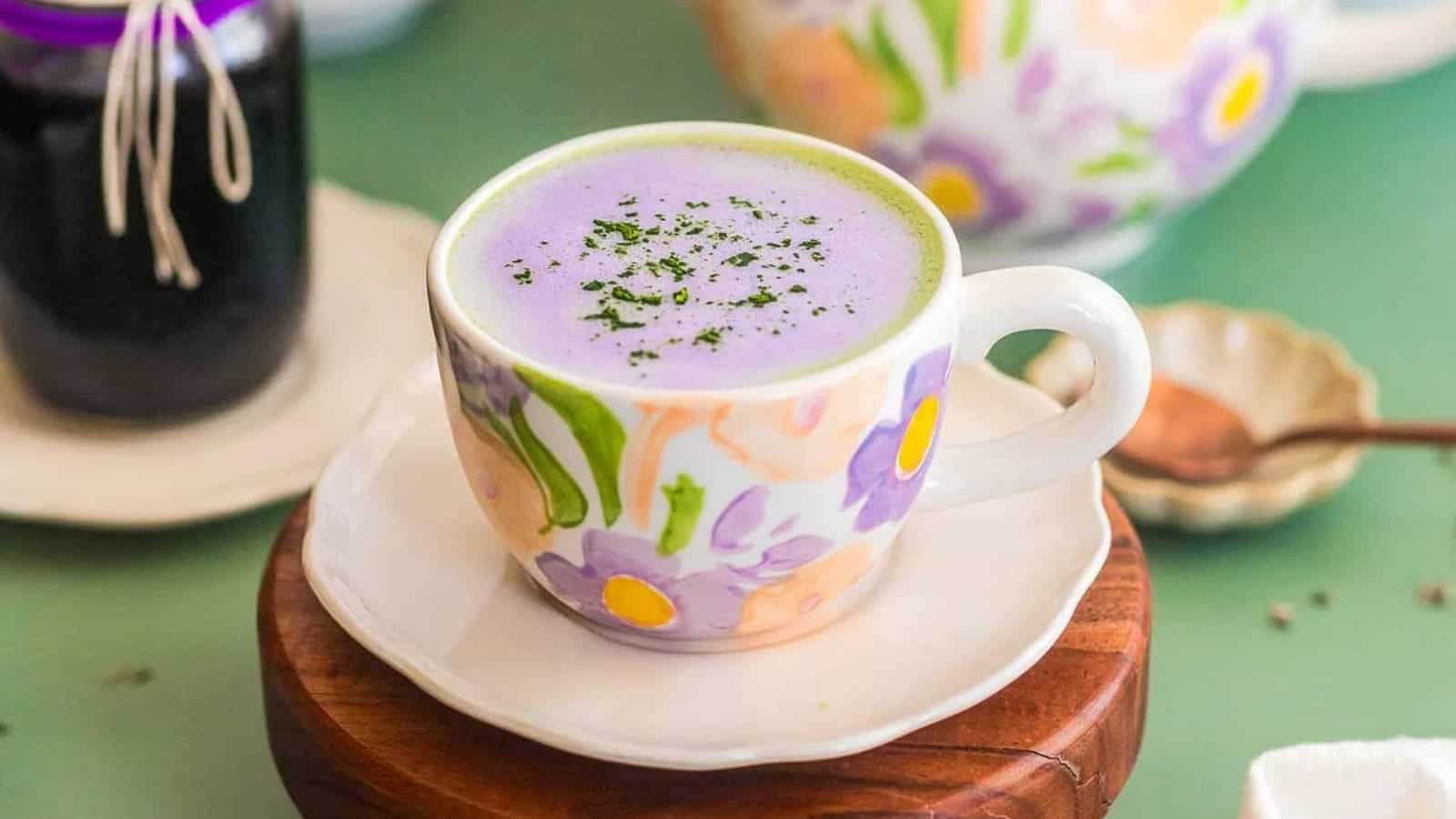 A floral teacup filled with purple matcha latte, garnished with green powder, on a saucer.