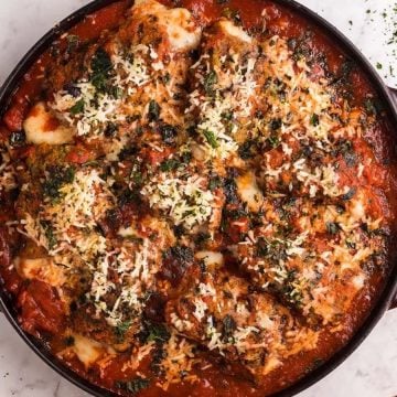 Baked chicken Parmesan in a round red dish, topped with melted cheese, herbs, and tomato sauce.