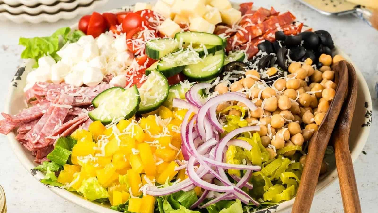 A bowl of chopped salad with lettuce, cucumbers, tomatoes, chickpeas, cheese, meats, olives, and onions.