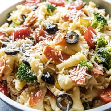 A bowl of pasta salad with broccoli, tomatoes, olives, pepperoni, and shredded cheese.