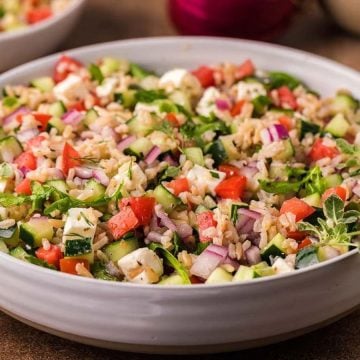 A bowl of colorful rice salad with chopped tomatoes, cucumbers, red onions, and fresh herbs.