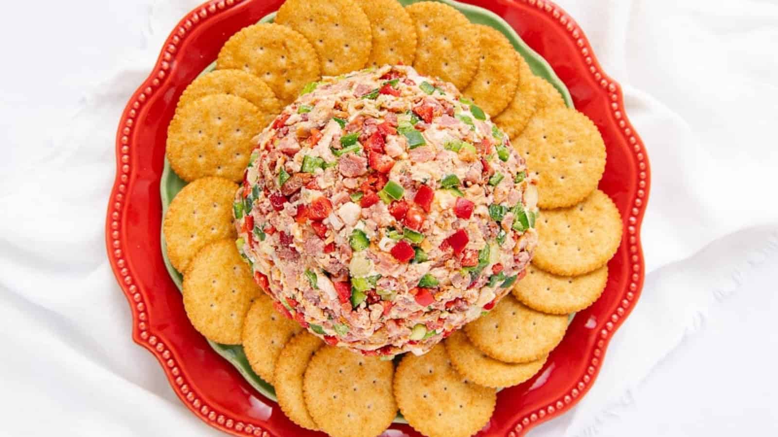 A colorful cheese ball with crackers arranged around it on a red and green plate.