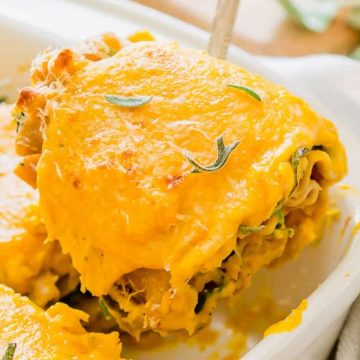 A slice of cheesy baked lasagna is being lifted from a casserole dish with a serving utensil.