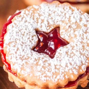 A round sandwich cookie with a star-shaped cutout, filled with red jam and dusted with powdered sugar.