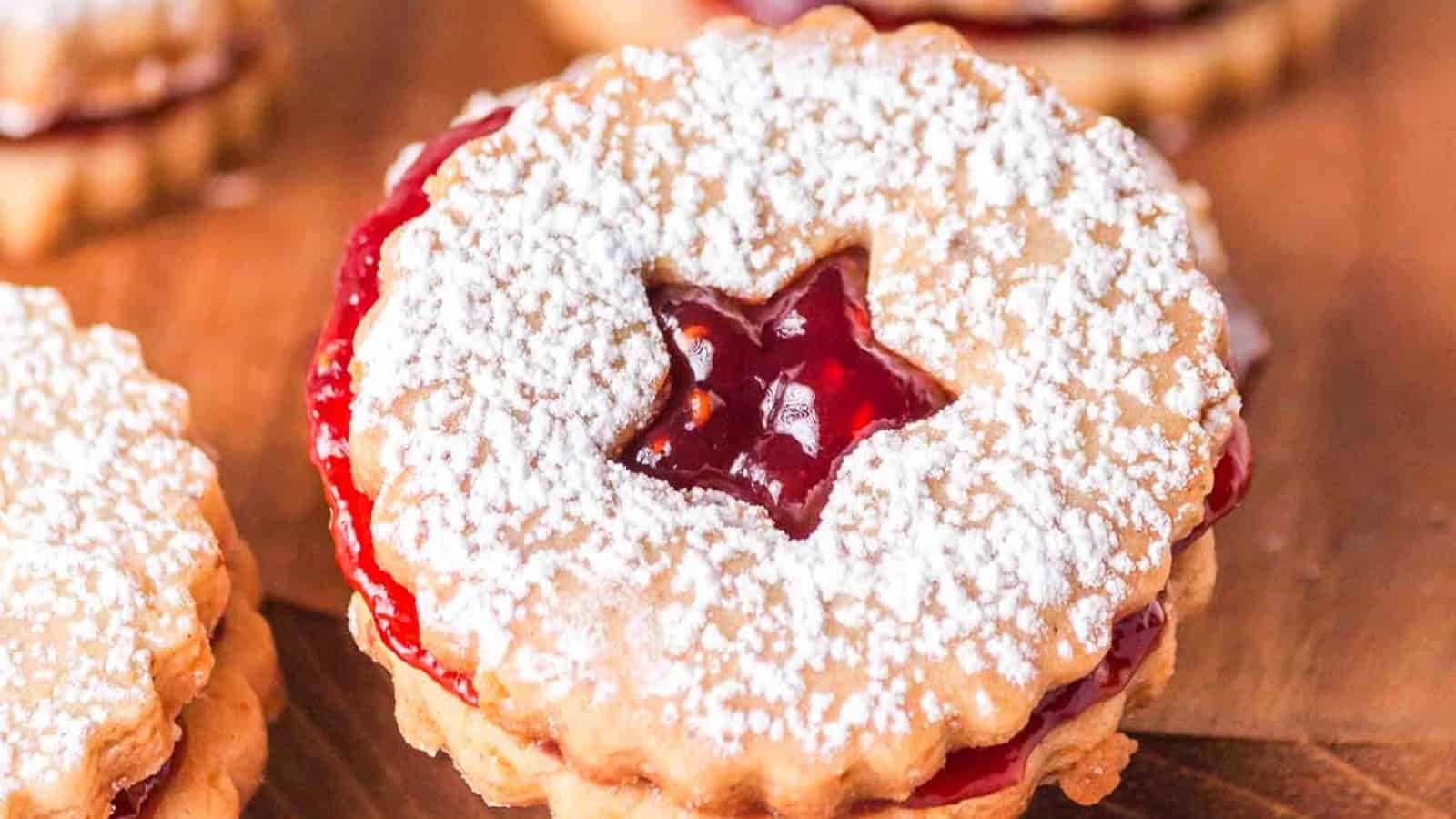 A round sandwich cookie with a star-shaped cutout, filled with red jam and dusted with powdered sugar.