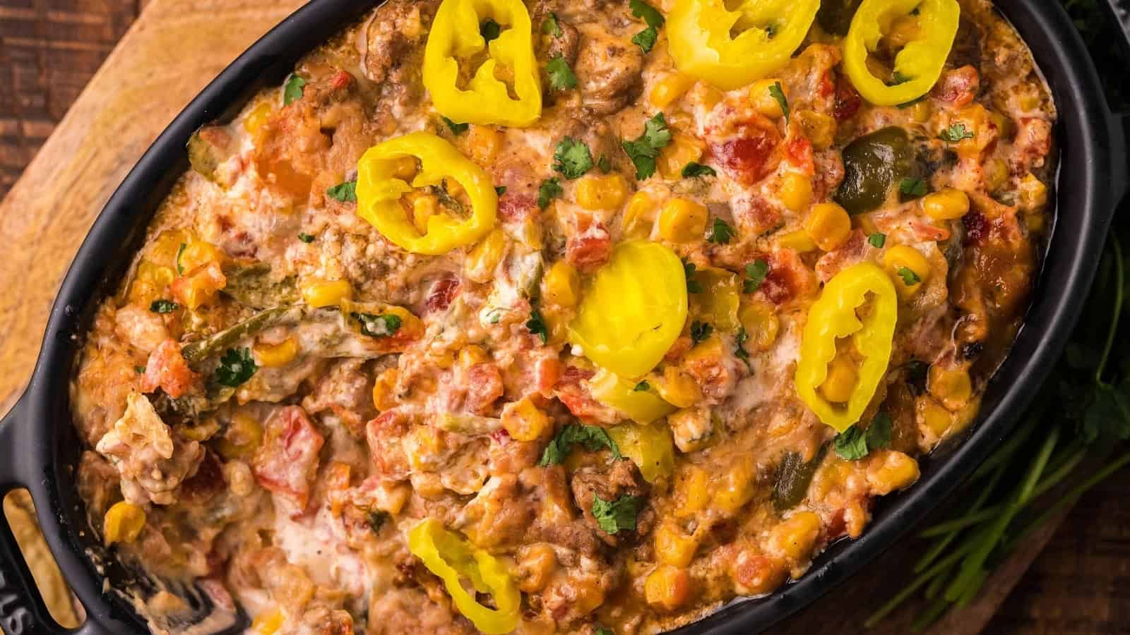 Cheesy baked casserole with diced tomatoes, corn, herbs, and sliced yellow peppers in a black dish.