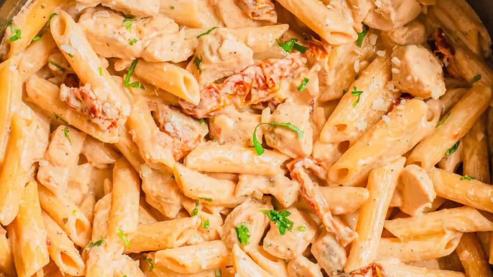 Creamy penne pasta with chicken pieces, sun-dried tomatoes, and fresh herbs garnished on top.