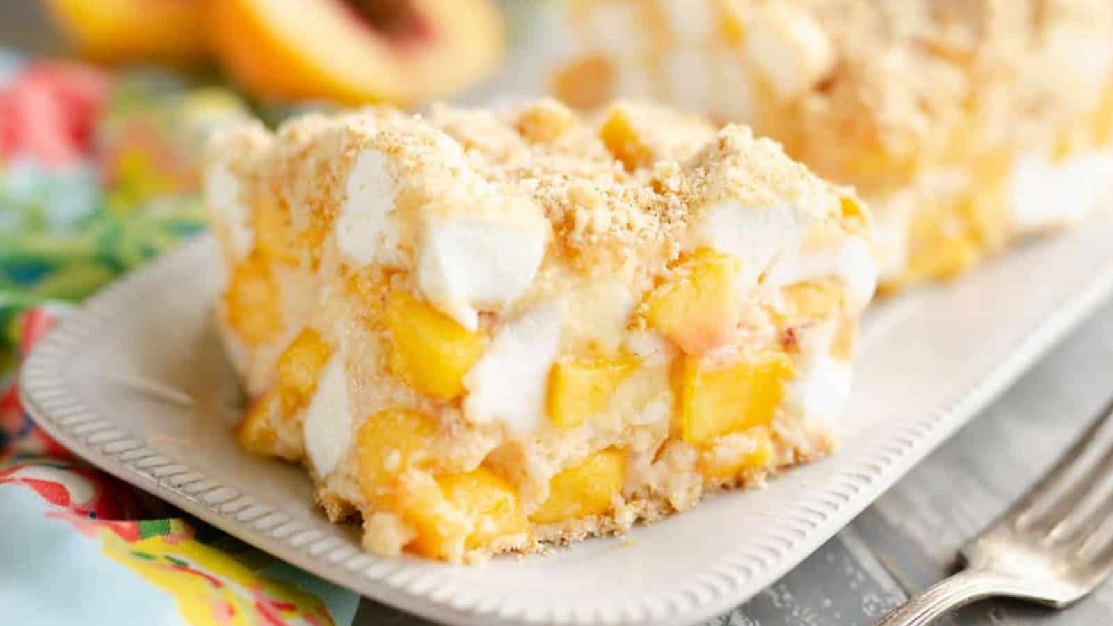 A slice of peach dessert with marshmallows and crumb topping on a white plate, colorful napkin beside it.
