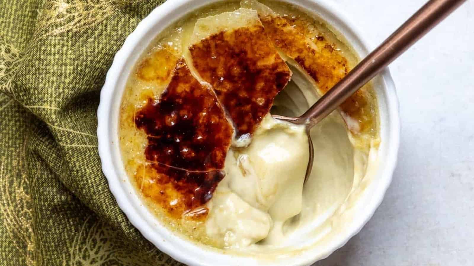 A spoon breaks into the caramelized sugar top of a cr&egrave;me br&ucirc;l&eacute;e in a white ramekin.