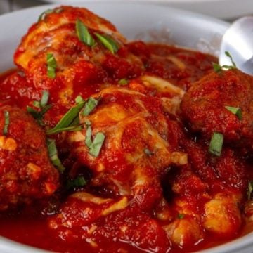 A bowl of spicy red tomato sauce with boiled eggs, garnished with chopped green herbs and a spoon on the side.