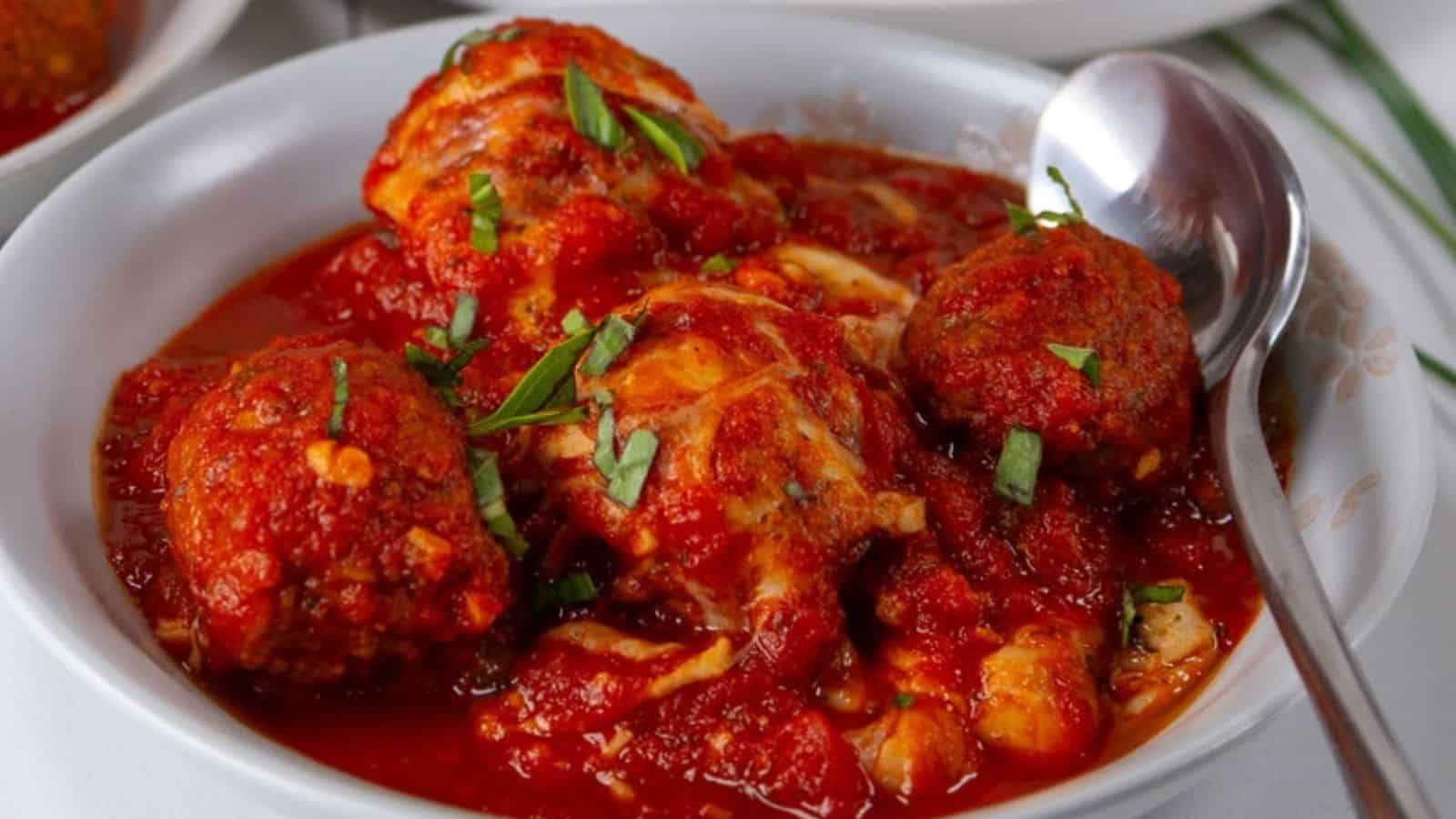 A bowl of spicy red tomato sauce with boiled eggs, garnished with chopped green herbs and a spoon on the side.