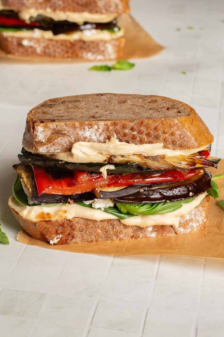 Veggie Hummus Sandwich with grilled eggplant, red pepper, fresh greens, and creamy hummus on rustic bread, served on parchment paper.