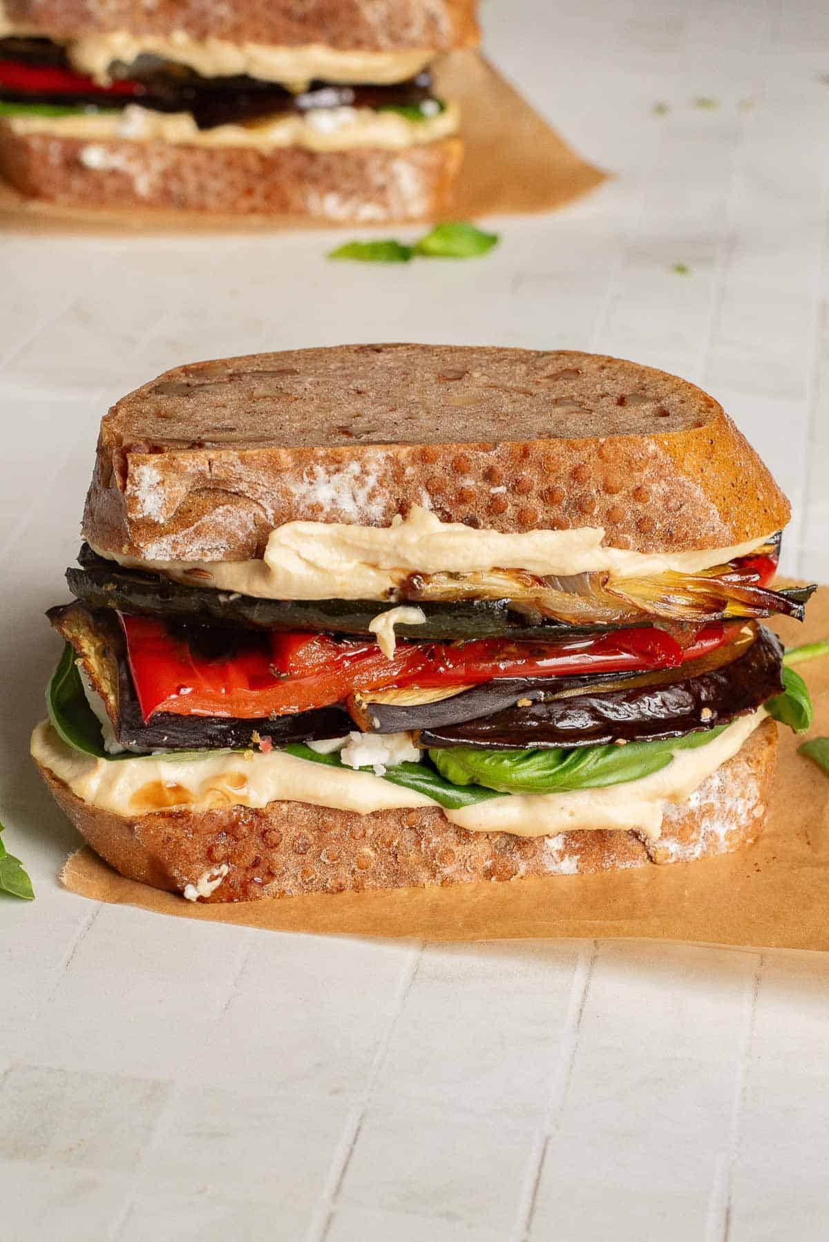 Veggie Hummus Sandwich with grilled eggplant, red pepper, fresh greens, and creamy hummus on rustic bread, served on parchment paper.