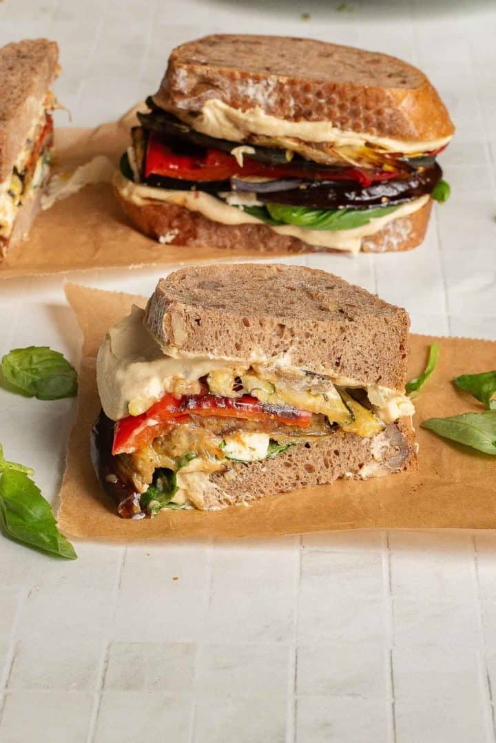 Three Veggie Hummus Sandwiches with grilled eggplant, red pepper, and hummus on whole grain bread, arranged on parchment paper.
