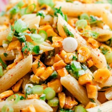 A bowl of penne pasta mixed with corn, chopped scallions, herbs, and spices.