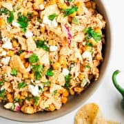 Bowl of Mexican street corn salad with tortilla chips, cheese, cilantro, and corn kernels.