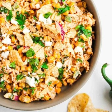 Bowl of Mexican street corn salad with tortilla chips, cheese, cilantro, and corn kernels.