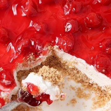 No-bake cherry cheesecake with a graham cracker crust in a dish, a spoonful served—a timeless treat inspired by vintage desserts.