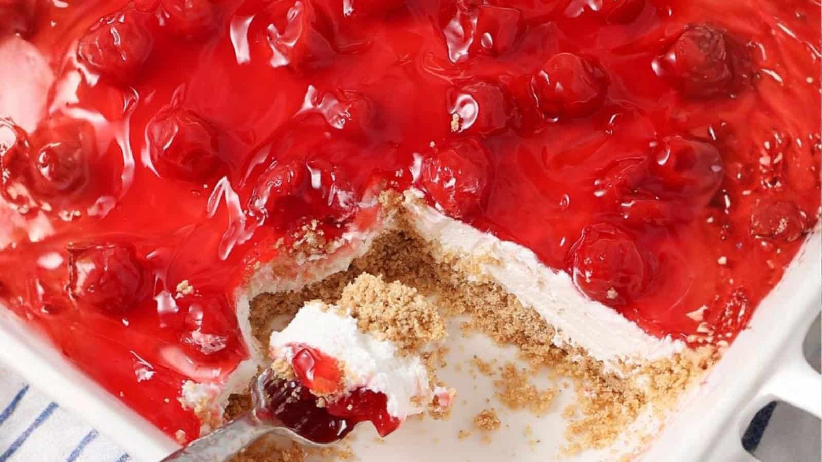 No-bake cherry cheesecake with a graham cracker crust in a dish, a spoonful served&mdash;a timeless treat inspired by vintage desserts.