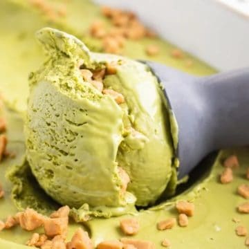A scoop of green matcha ice cream with toffee bits being served from a container.