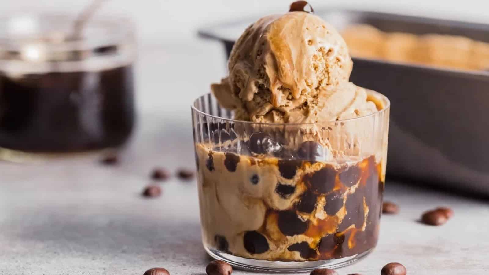 A glass of coffee ice cream with boba pearls and syrup, surrounded by scattered coffee beans.