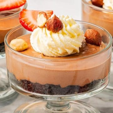 Chocolate mousse dessert in a glass, topped with whipped cream, strawberries, and hazelnuts.