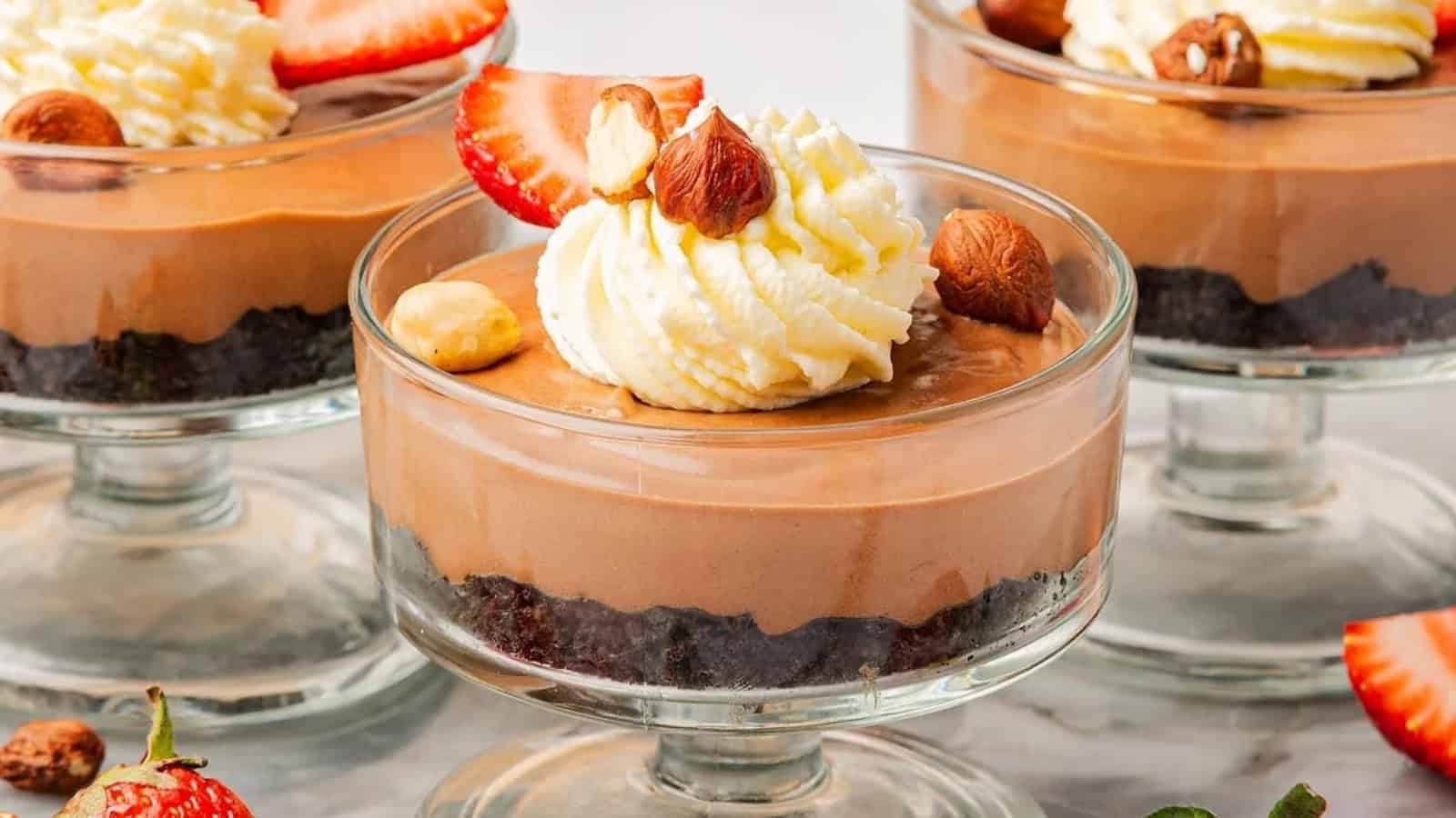 Chocolate mousse dessert in a glass, topped with whipped cream, strawberries, and hazelnuts.