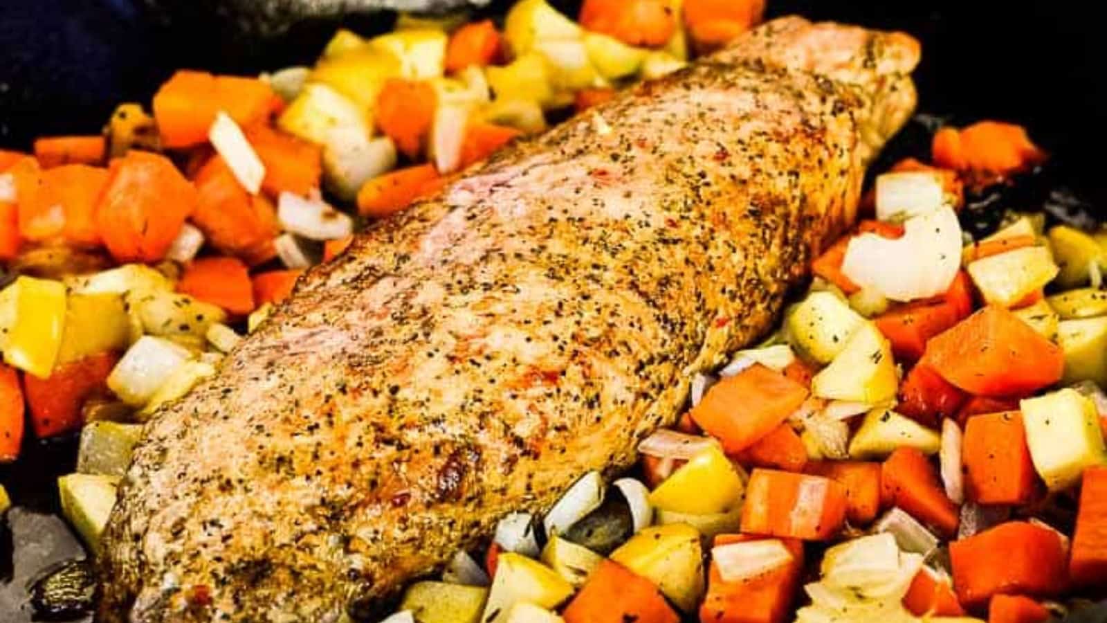 Cooked seasoned pork surrounded by diced vegetables in a black skillet on a wooden table.