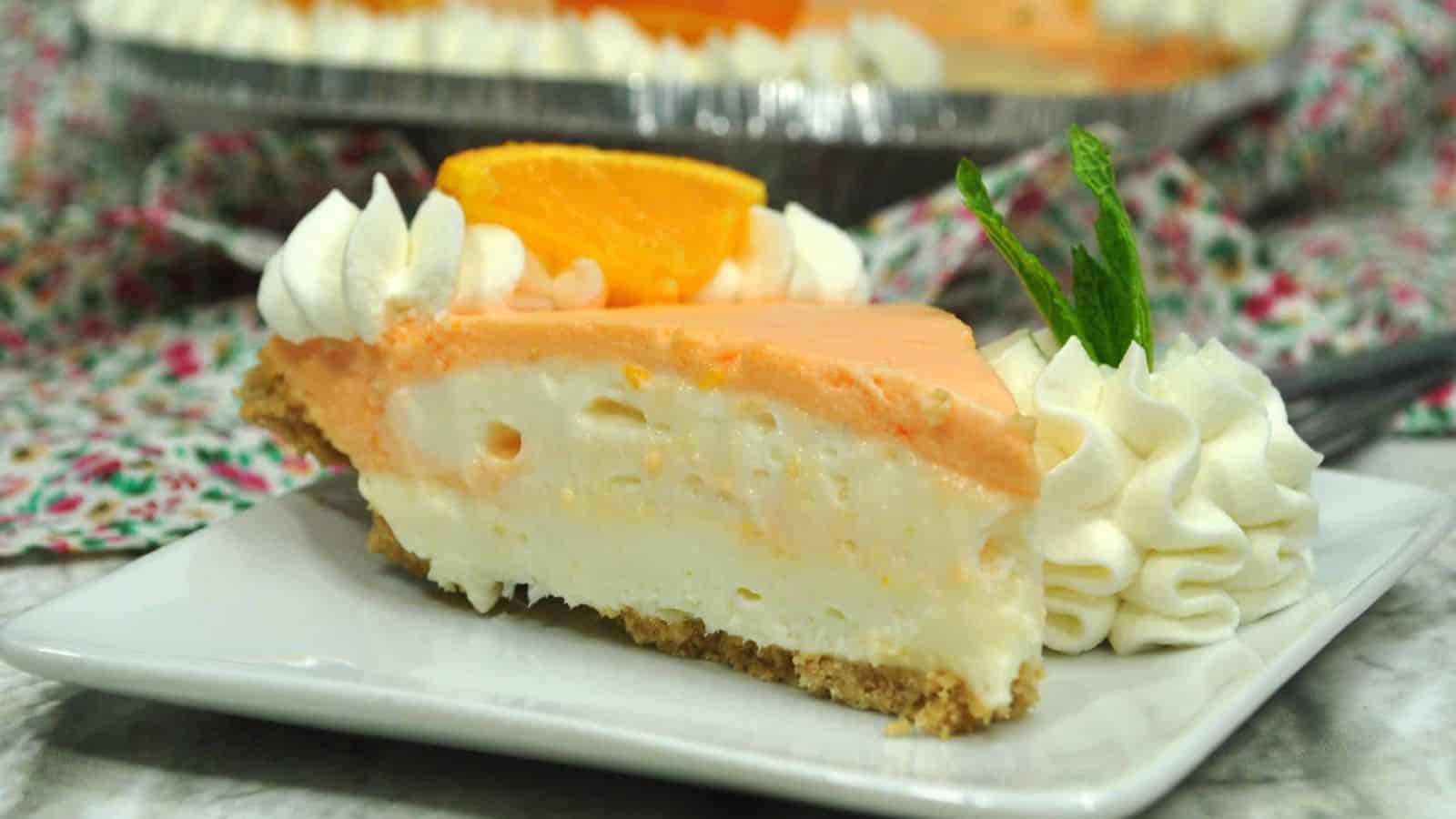 A slice of creamy orange pie with whipped cream and an orange slice, served on a white plate.