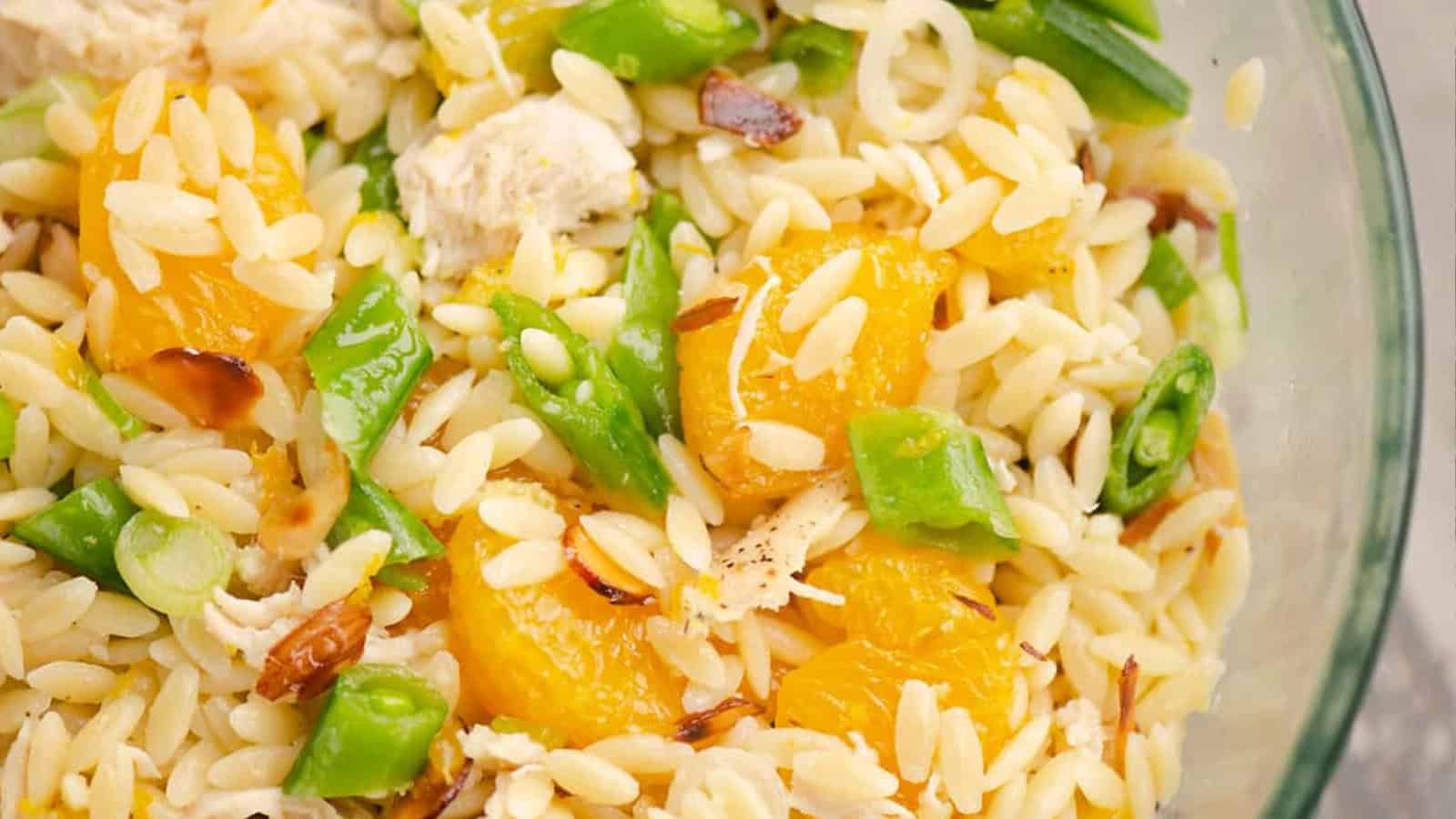 Orzo pasta salad with mandarin oranges, green beans, and toasted almonds in a clear glass bowl.