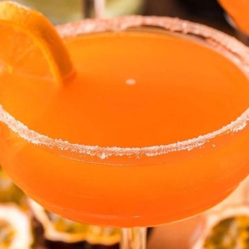 A bright orange cocktail with a sugar rim and an orange slice garnish on the glass.