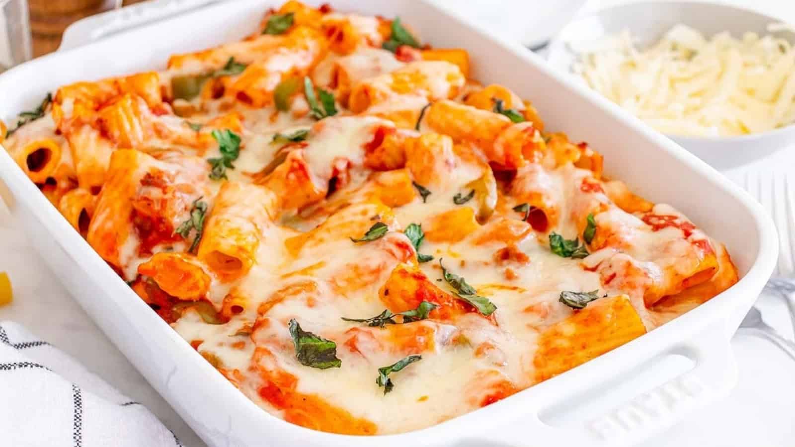 Baked pasta with melted cheese, tomato sauce, and fresh basil in a white casserole dish.