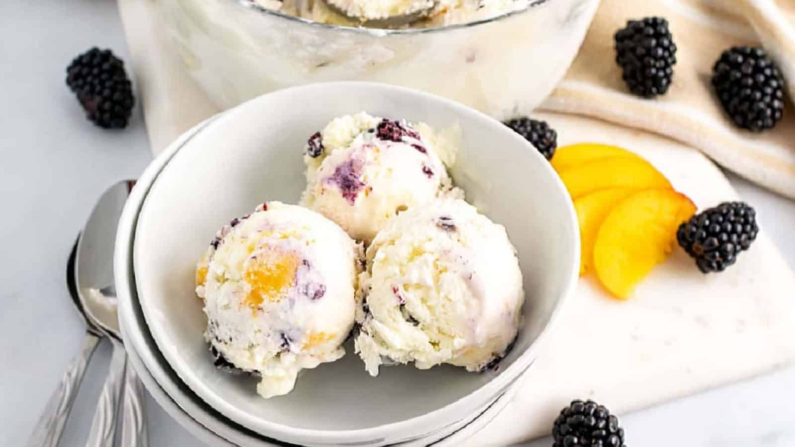 Peach and blackberry ice cream scoops in white bowls.