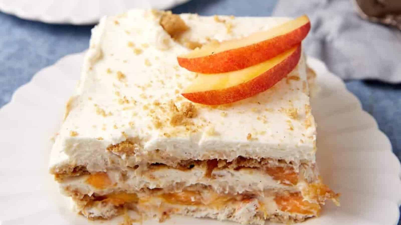 A layered peach dessert topped with whipped cream and peach slices on a white plate.