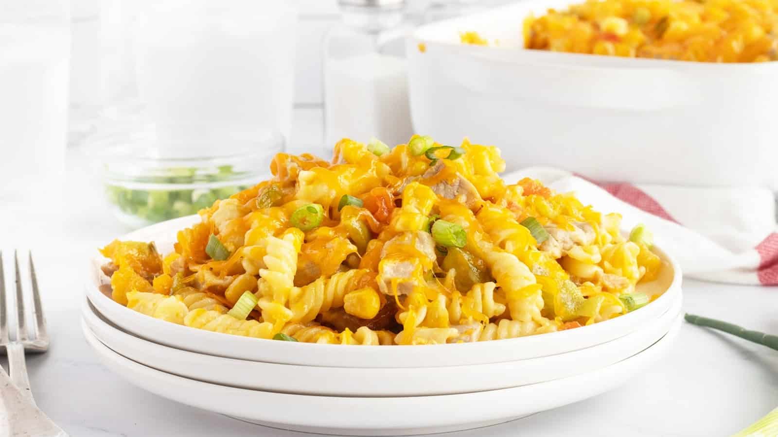 A plate of cheesy rotini pasta casserole topped with green onions, with a baking dish in the background.